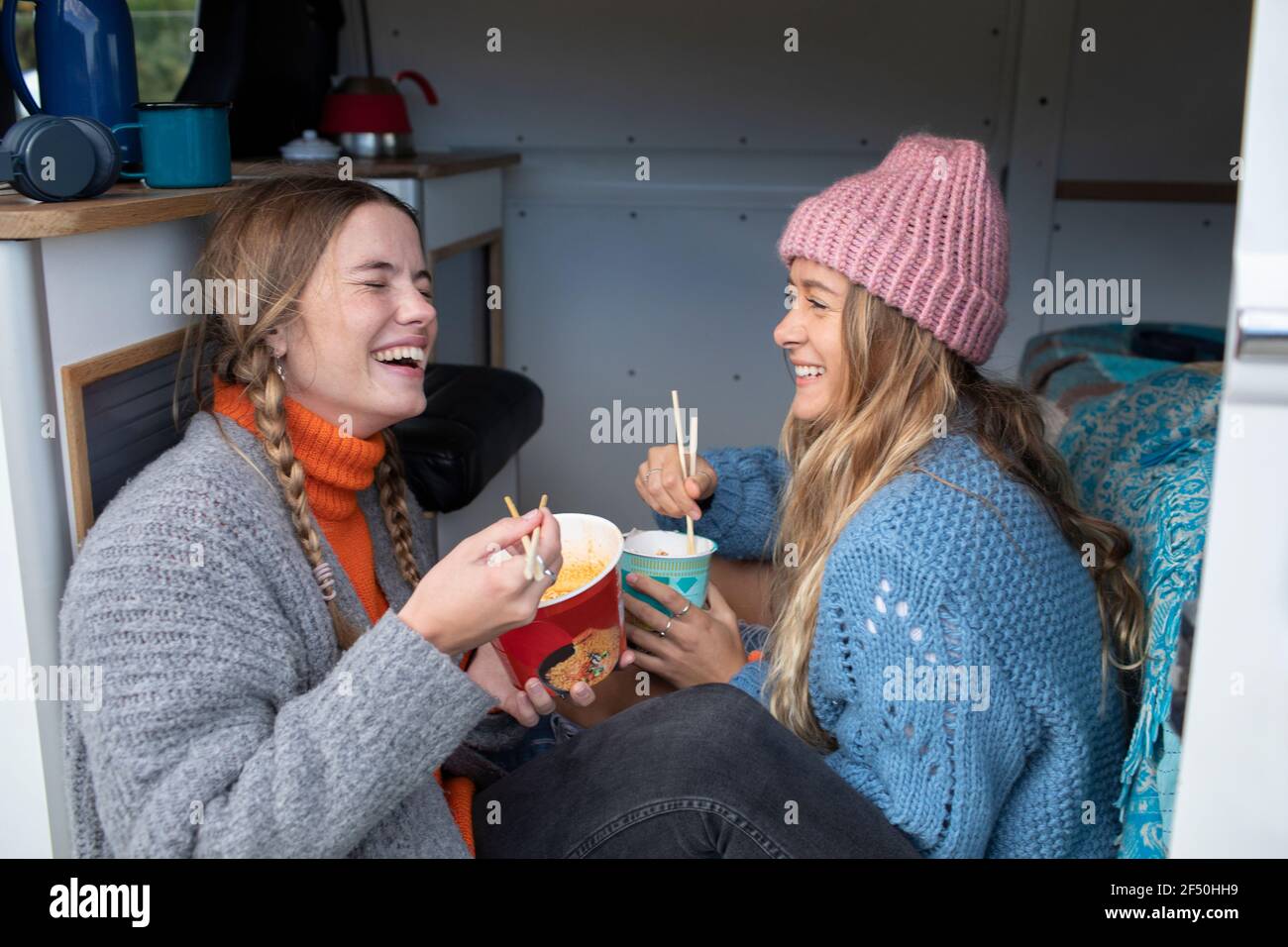 Happy young women friends eating instant noodles in camper van Stock Photo
