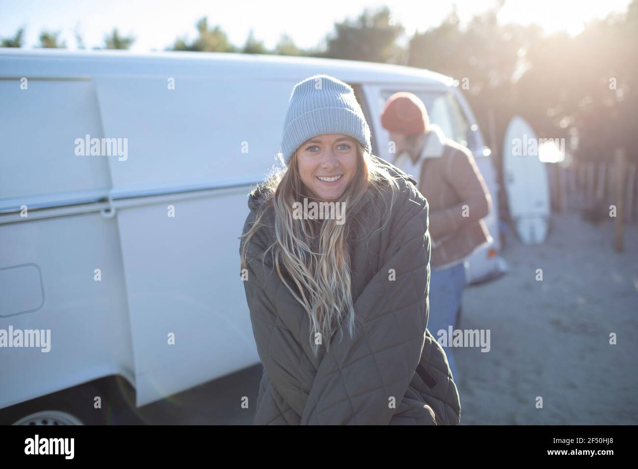 Portrait happy young female surfer in coat and hat outside sunny van Stock Photo