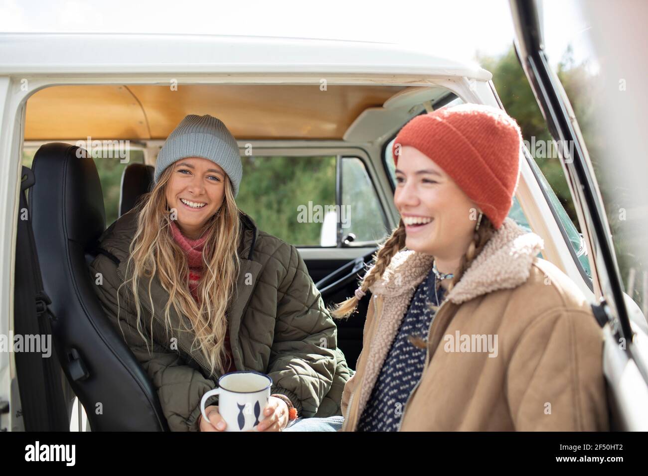 Happy young women friends with coffee in camper van doorway Stock Photo