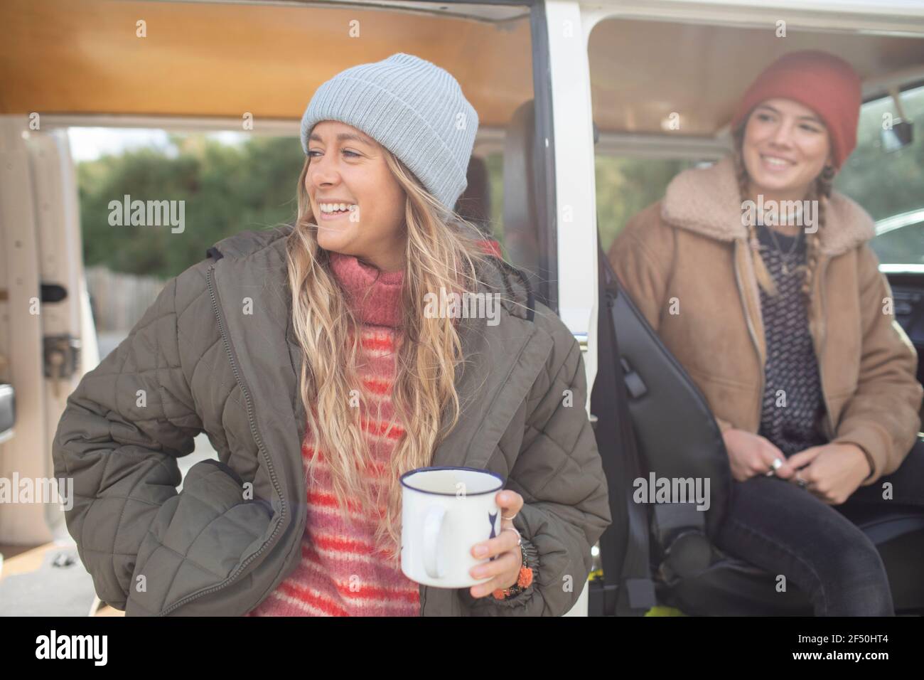 Happy young women friends drinking tea at camper van doorway Stock Photo