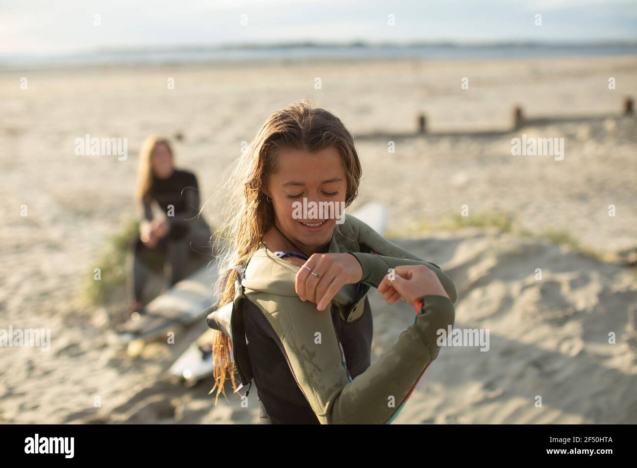 Young female surfer putting on wet suit on sunny summer beach Stock Photo