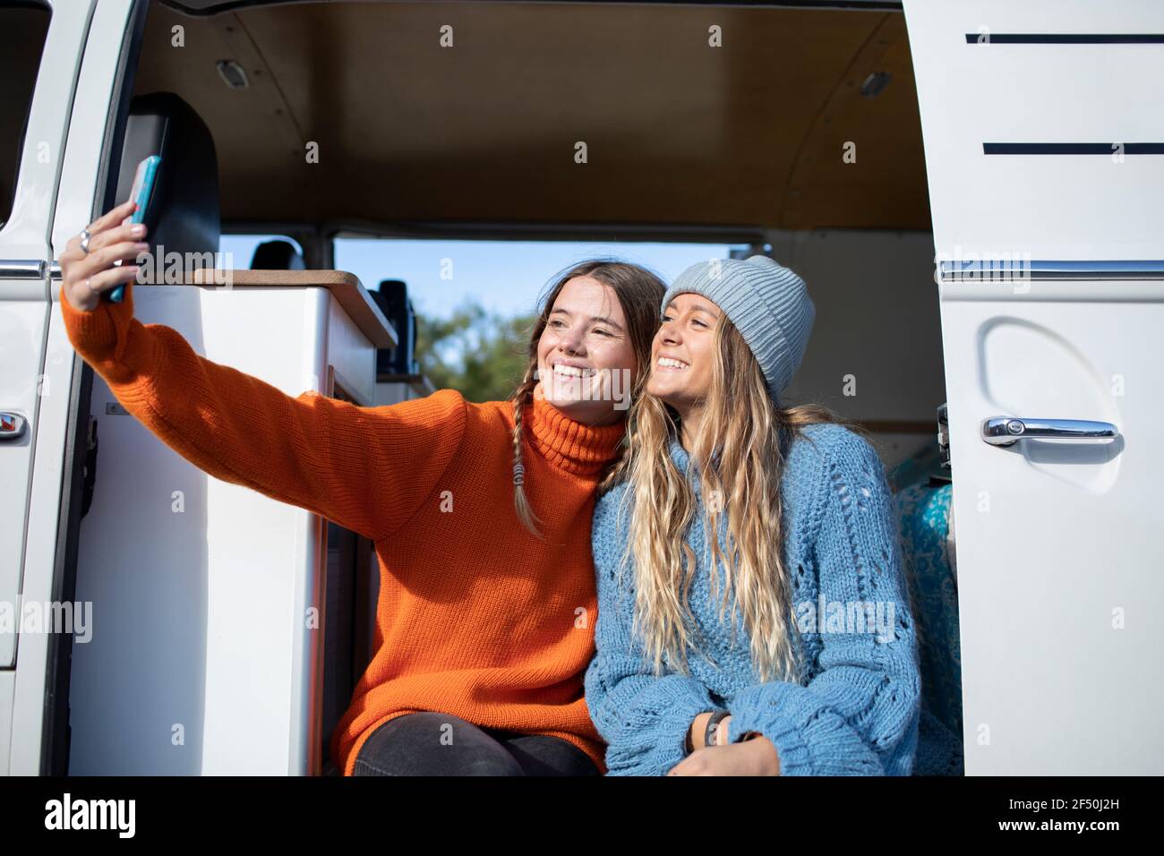 Happy young women friends taking selfie in camper van doorway Stock Photo