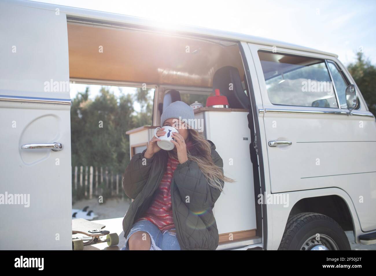 Young woman drinking coffee in sunny doorway of camper van Stock Photo