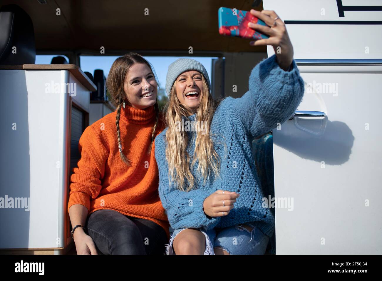 Happy young women friends taking selfie in sunny camper van doorway Stock Photo