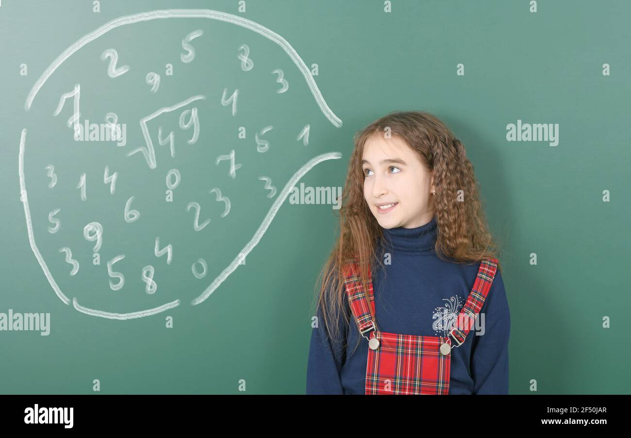 Pre-adolescent girl ponders and looks at the chalk speech bubble. Thinking displayed mathematical symbols. High resolution photo. Full depth of field. Stock Photo