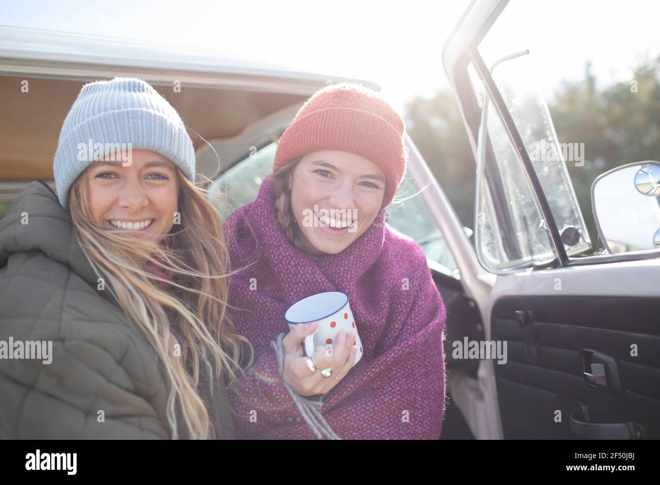 Portrait happy young women friends with coffee in camper doorway Stock Photo