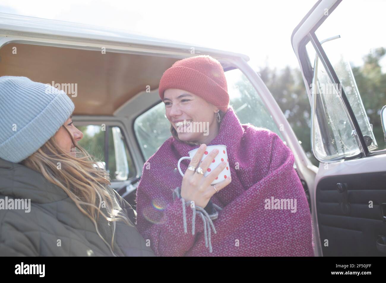 Happy young women friends drinking tea at sunny van doorway Stock Photo