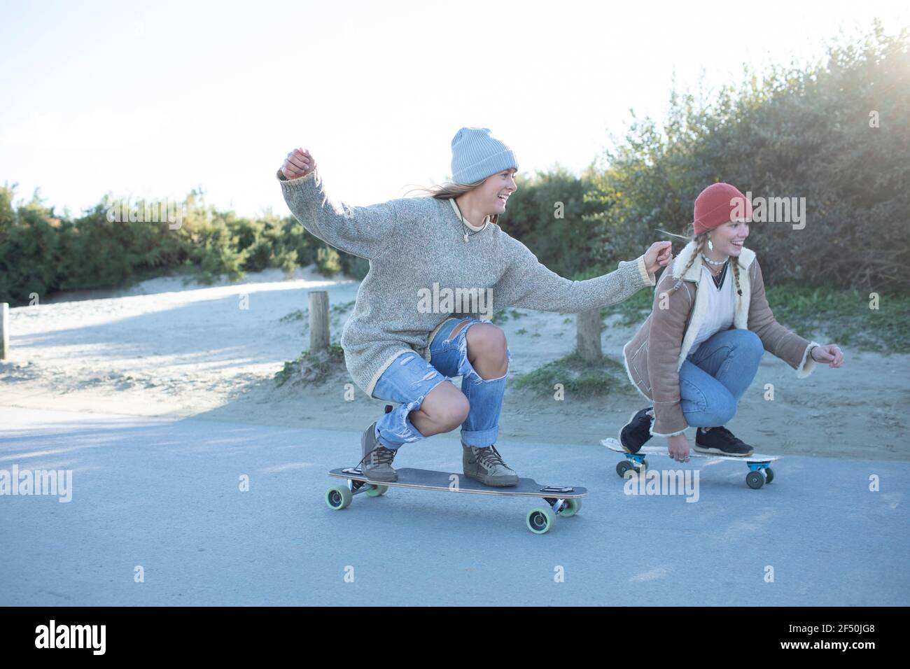 Carefree young women friends skateboarding on beach boardwalk Stock Photo