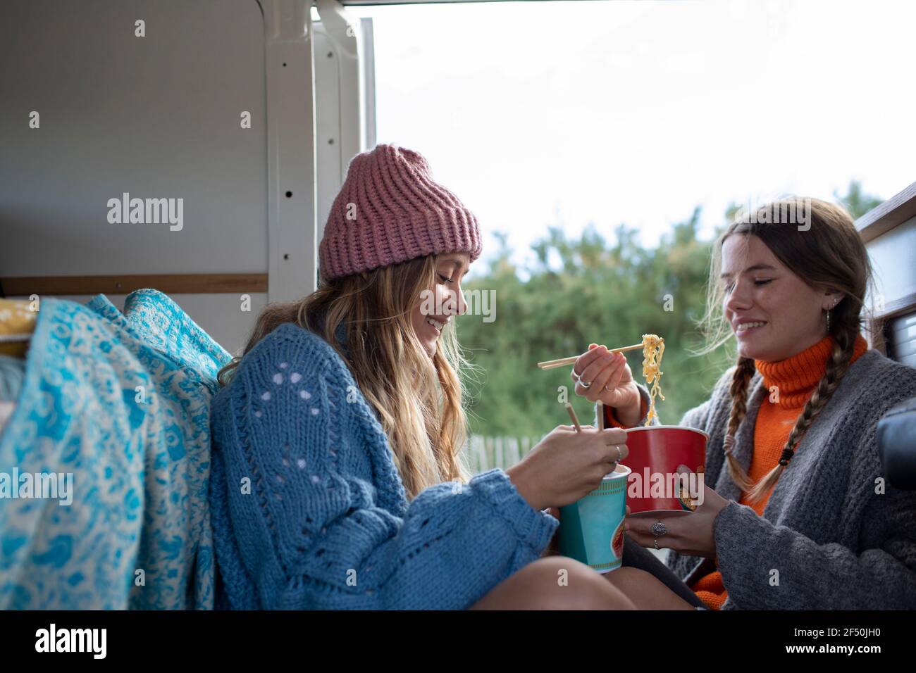 Young women friends eating instant noodles in camper van Stock Photo