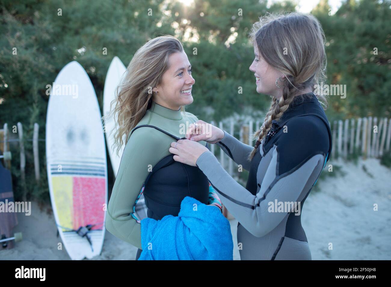 Happy young women friends putting on wet suits on beach Stock Photo