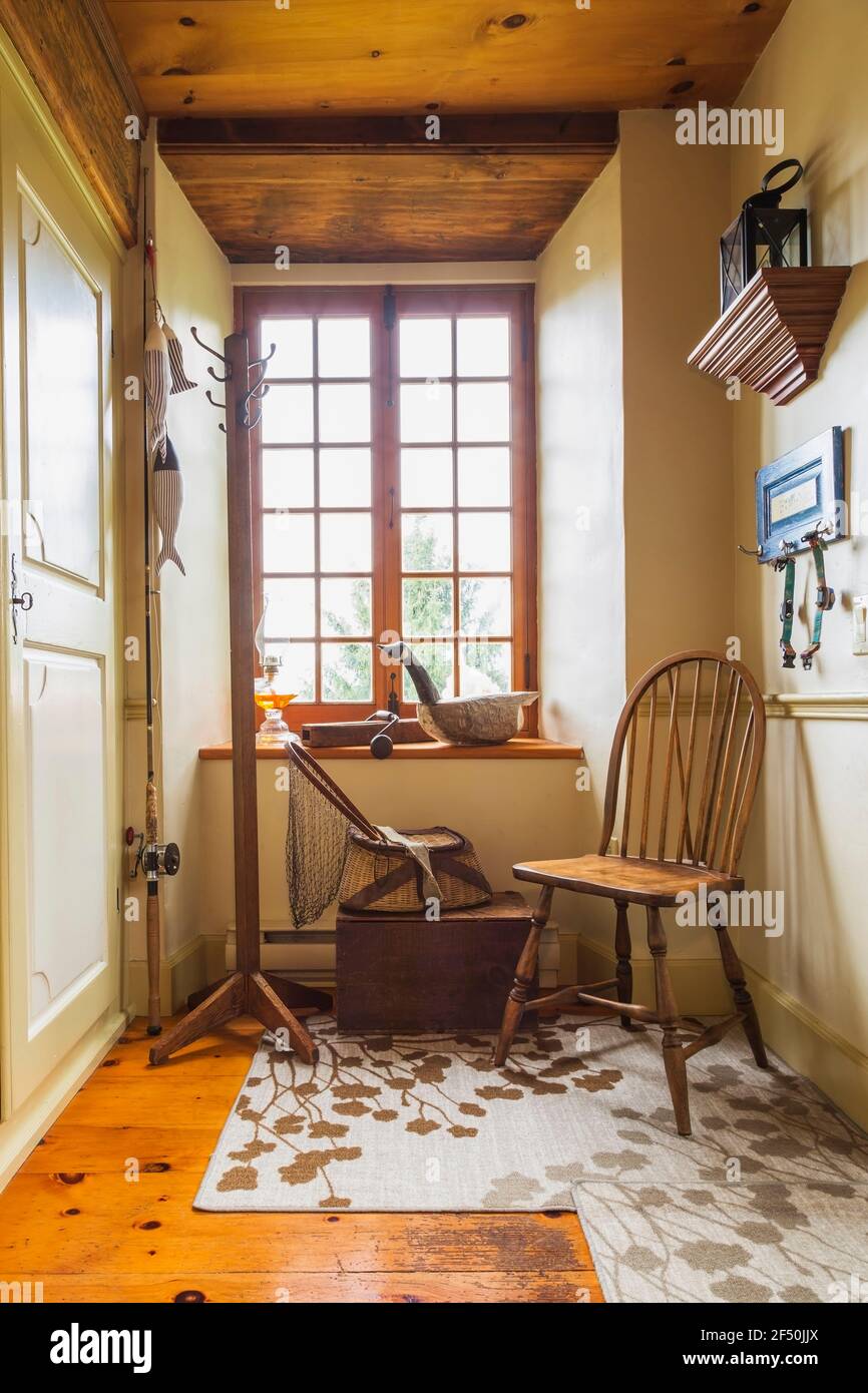 Antique wooden chair, fishing tackle, carved geese decoy on windowsill in entryway with rugs and pine wood floorboards inside an old circa 1735 house Stock Photo