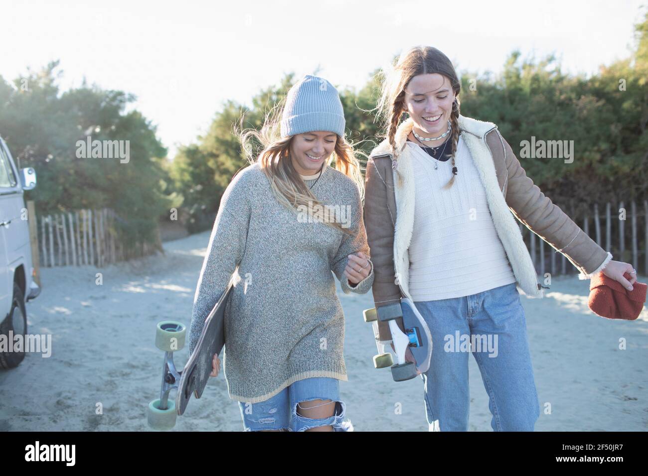 Happy young women friends with skateboards on sunny beach path Stock Photo