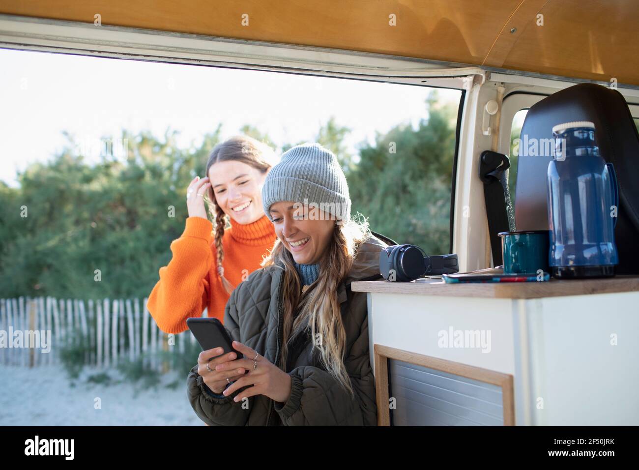 Young women friends using smart phone in camper van doorway Stock Photo