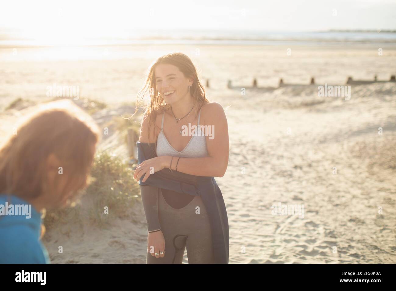 Happy young female surfer removing wet suit on sunny beach Stock Photo