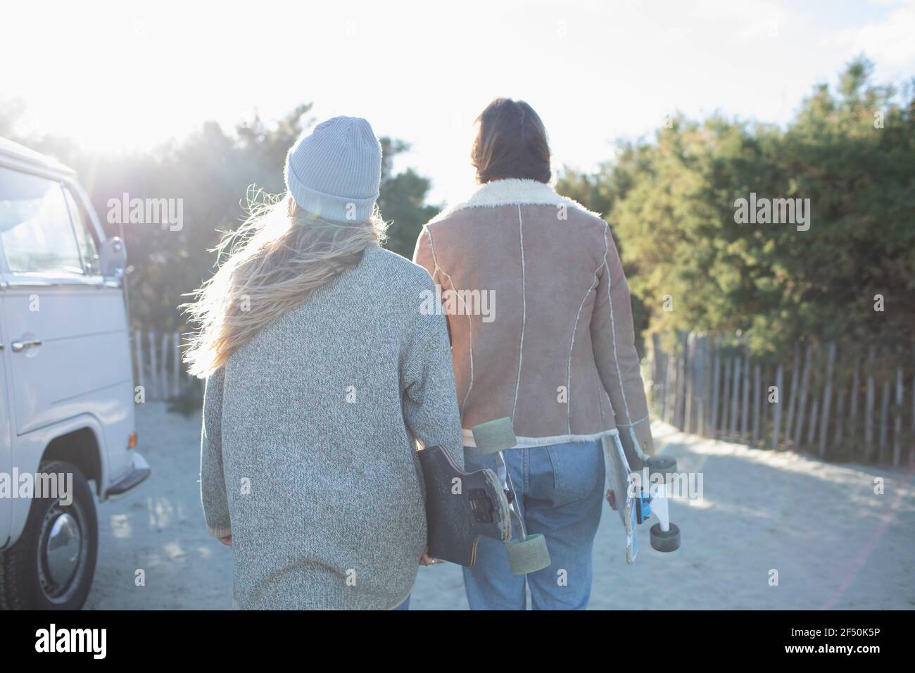 Young women friends with skateboards walking on sunny beach path Stock Photo