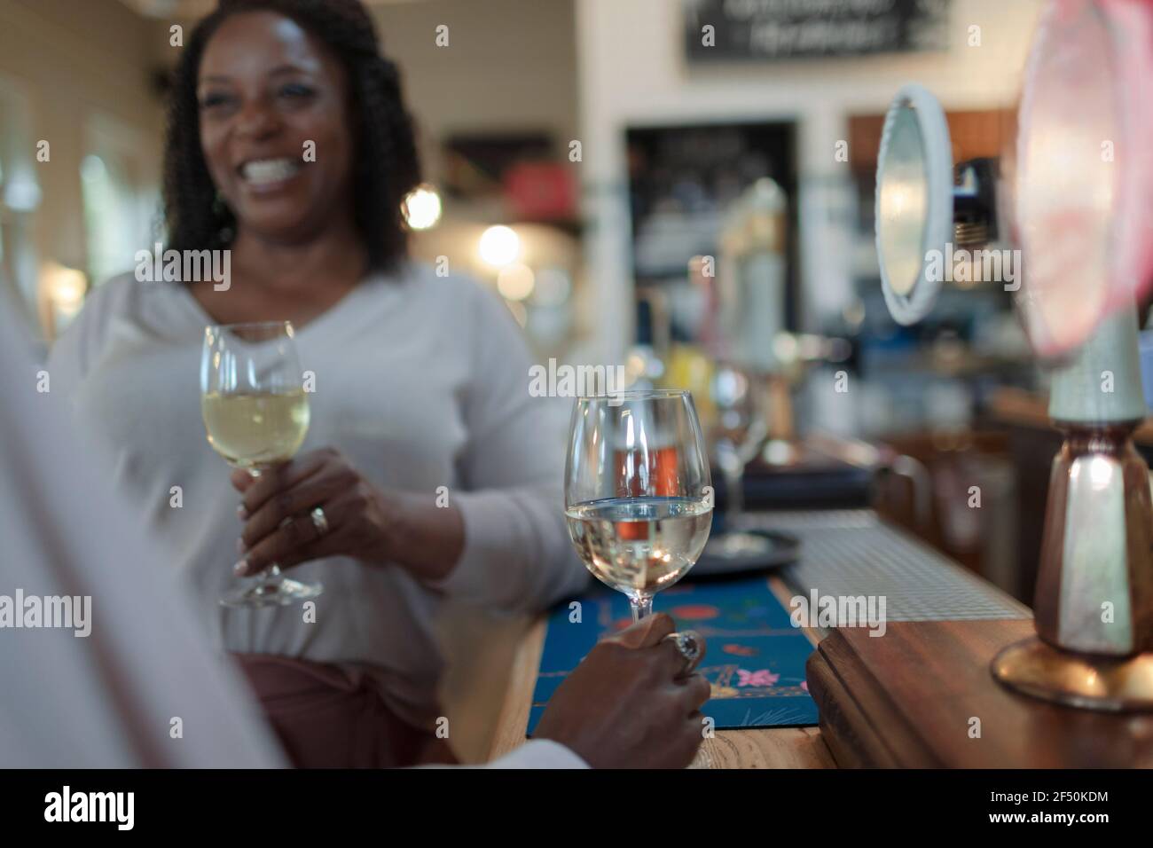Happy woman drinking white wine with friend in bar Stock Photo