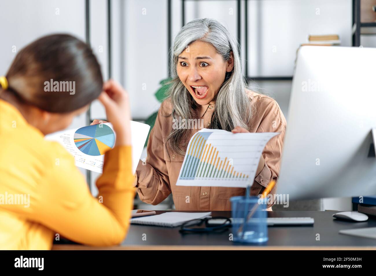 Annoyed angry disgruntled mature gray-haired Asian woman, chief of an employee, manager, in her office, scolds and shouts at a subordinate, shows an error in a report, gestures with her hands Stock Photo