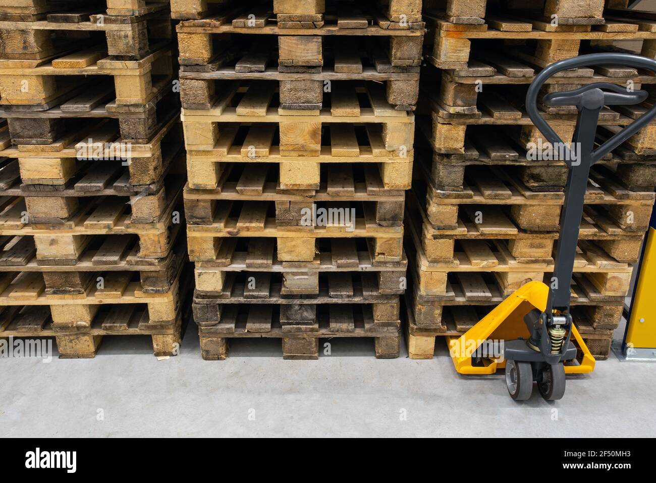 Hand pallet truck with stack of wooden pallets. Warehouse equipment