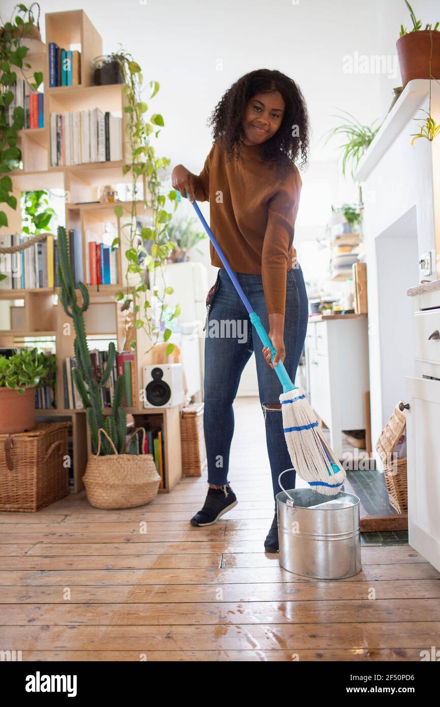 Portrait happy young woman mopping hardwood floor in apartment Stock Photo
