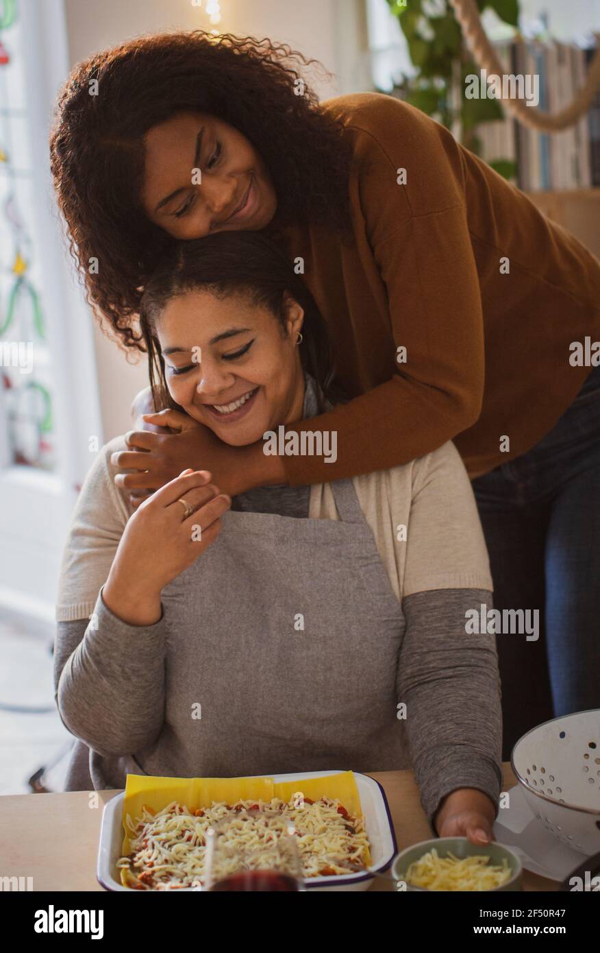 Affectionate mother and daughter hugging and making lasagna Stock Photo