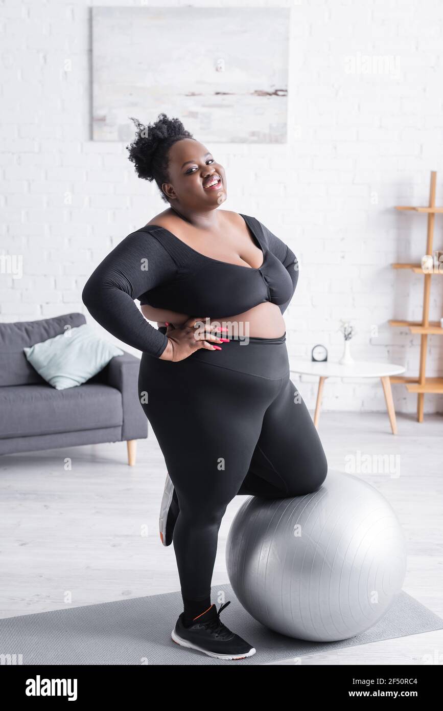 cheerful african american plus size woman in sportswear leaning on