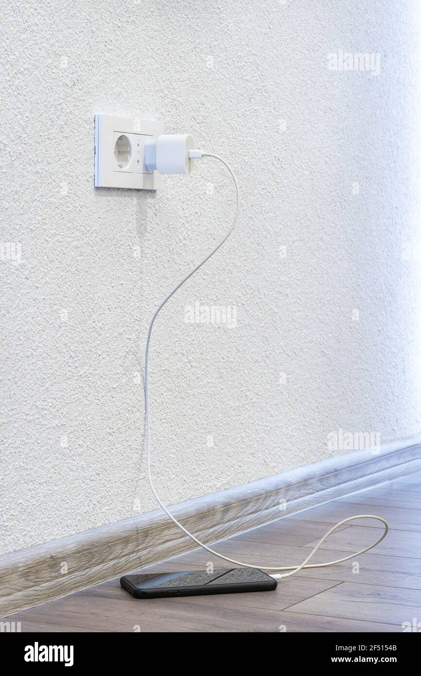 A charger in the socket that charges a mobile phone that stands on the floor Stock Photo