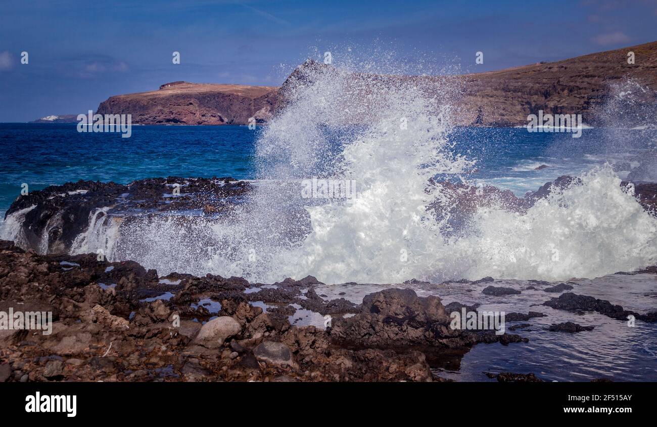 Wide shot of a rocky beach with waves breaking on the rocks on a sunny day Stock Photo