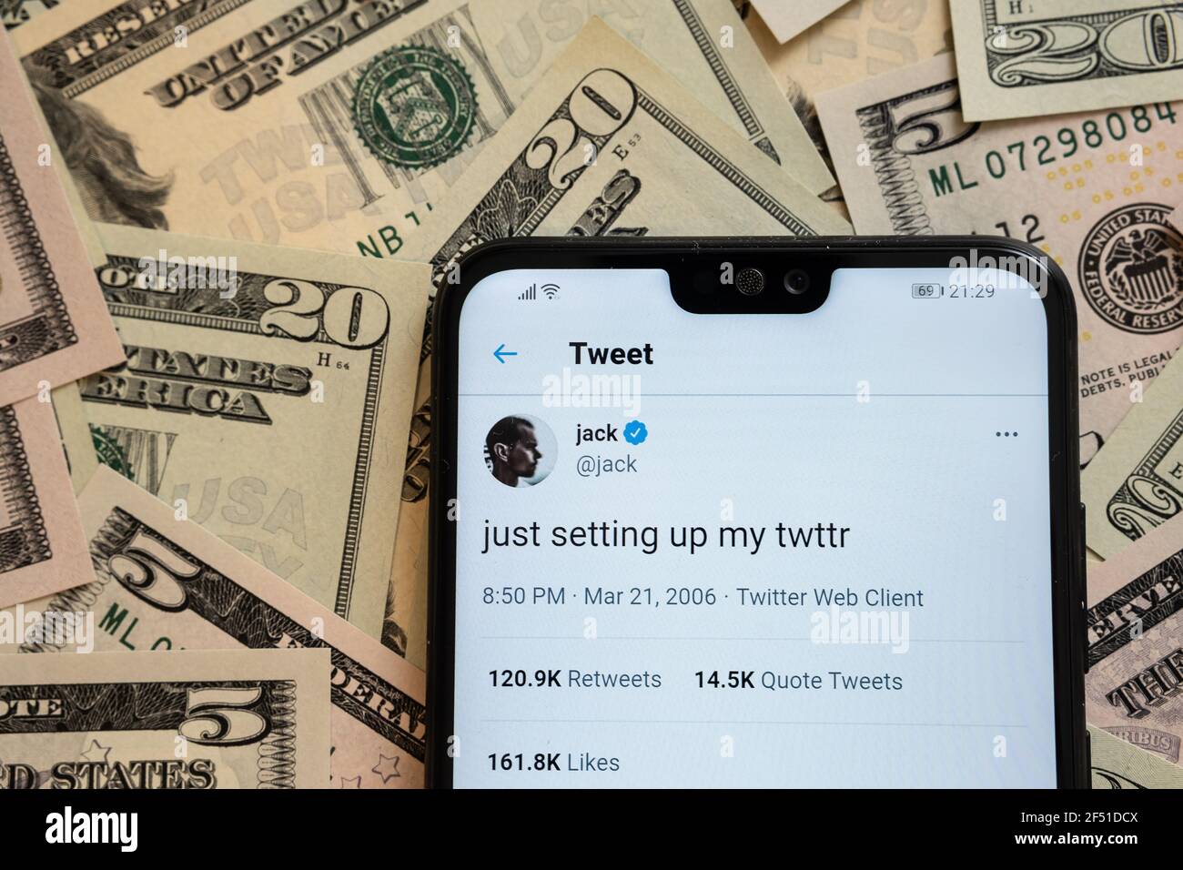 Smartphone with Jack Dorsey's tweet 'just setting up my twttr' placed on dollar bills.  First ever tweet sold as a non fungible token (NFT). Concept. Stock Photo
