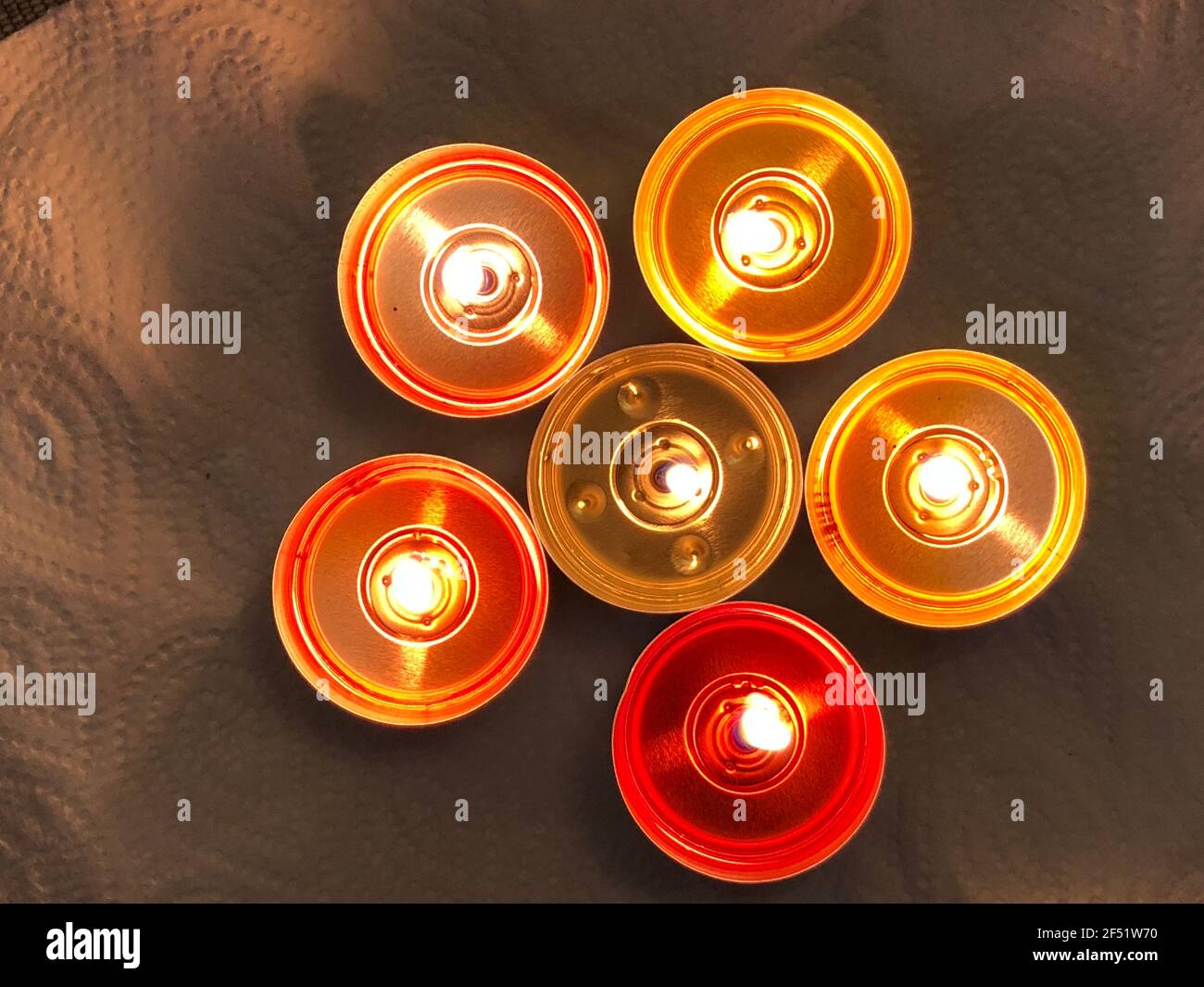 Lighted candles - flame.  Small heaters in a dark room. A few colored candles on a table. Candle flame on a dark background. Christmas celebration. Stock Photo