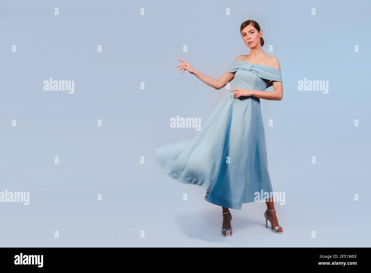 full shot of pretty young stylish blonde french girl in blue dress presenting your product. Isolated on blue background. Expressive facial expressions Stock Photo