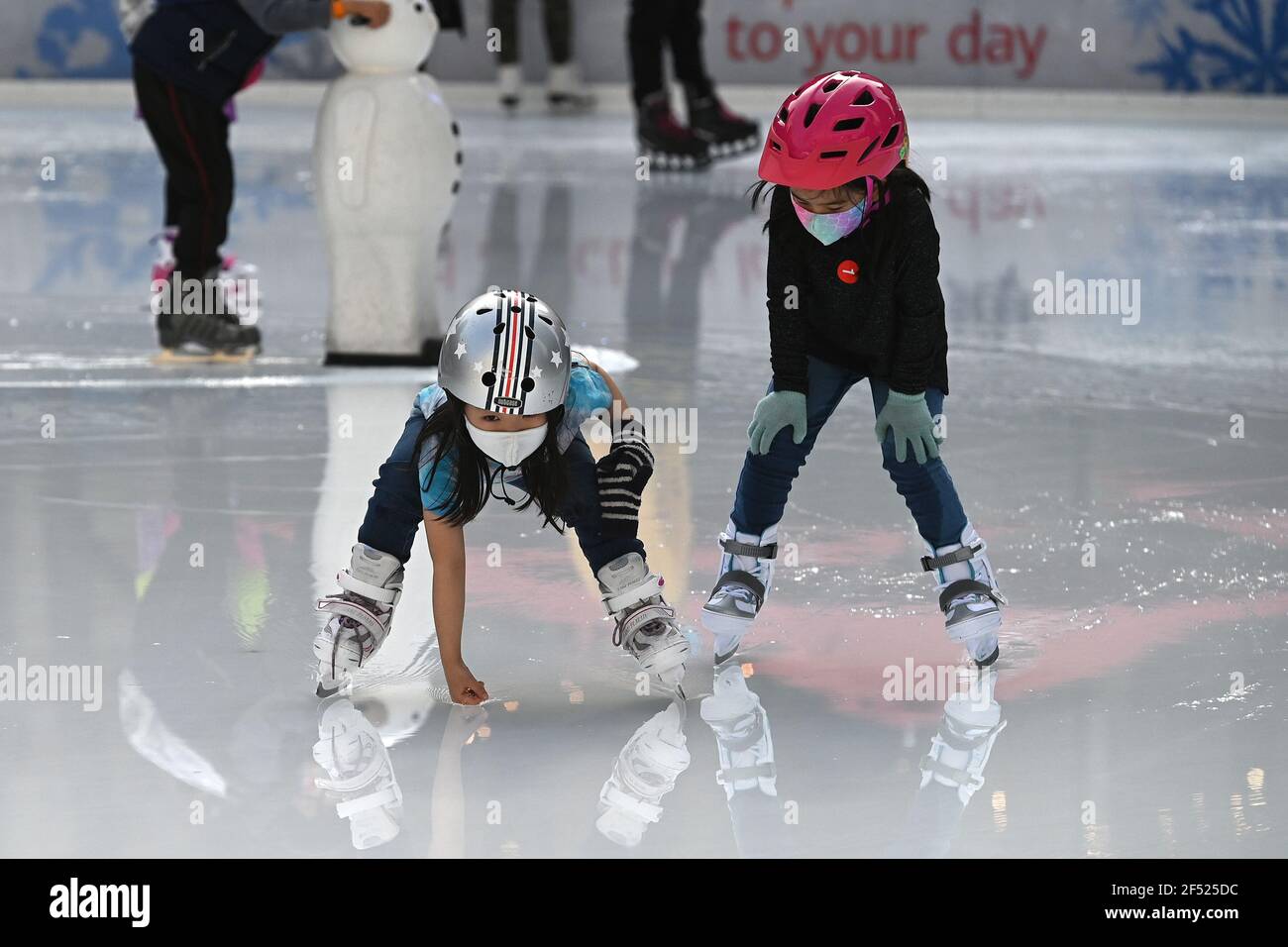 A young skater reaches down to run her hand through melted ice at the ...