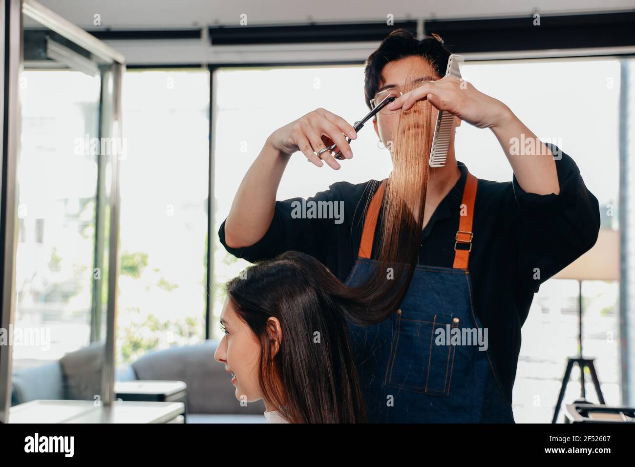 Young male Asian hairdresser concentrating on work while cutting and