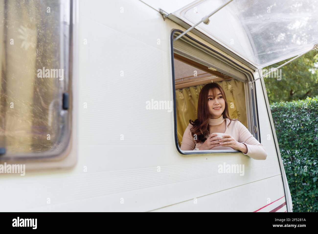 happy young woman drinking coffee at window of a camper RV van