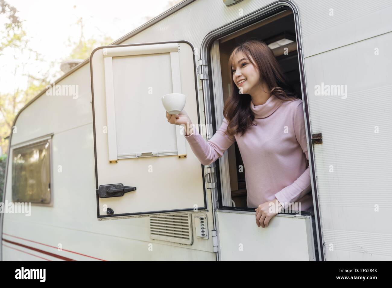 happy young woman drinking coffee at window of a camper RV van