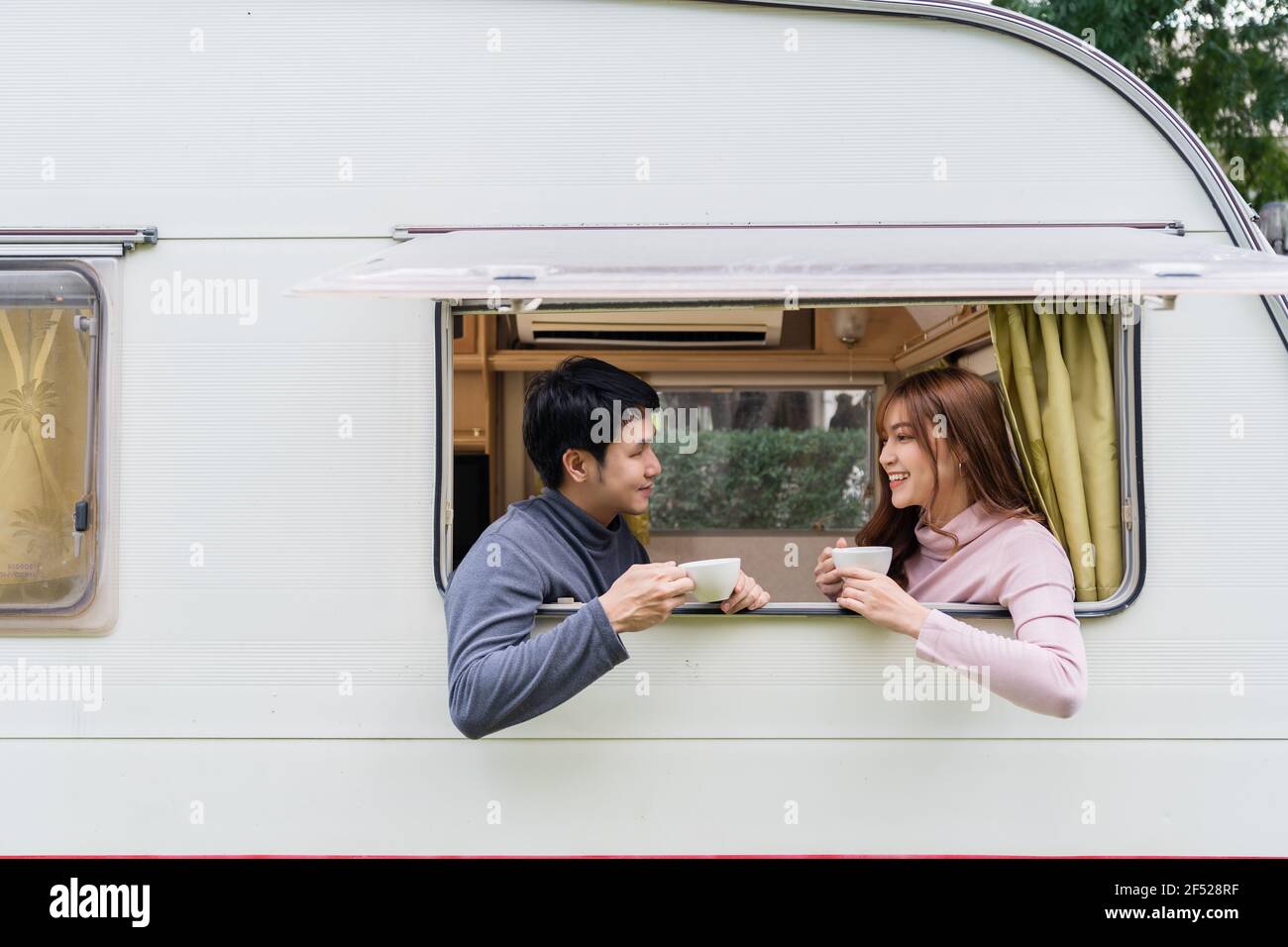 happy young couple drinking coffee at window of a camper RV van
