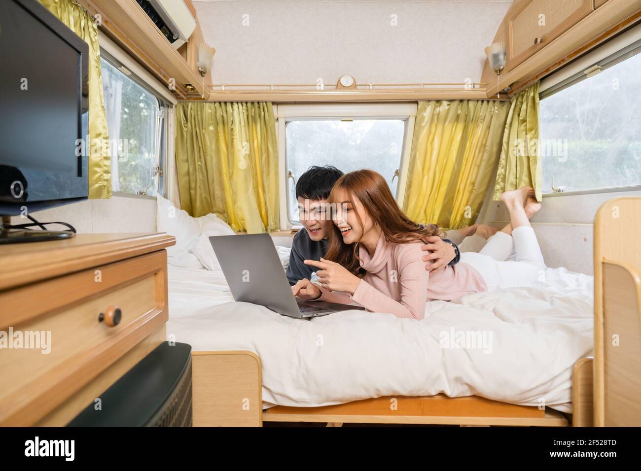 young couple using laptop computer on bed of a camper RV van motorhome Stock Photo