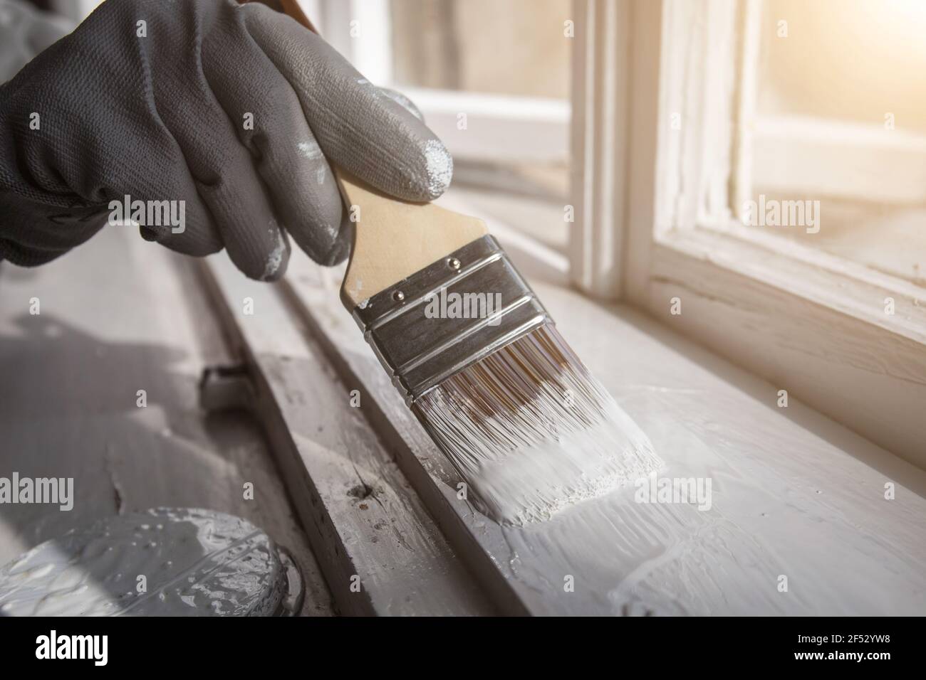 Painting wooden window with white color. Brush in hand with grey glove