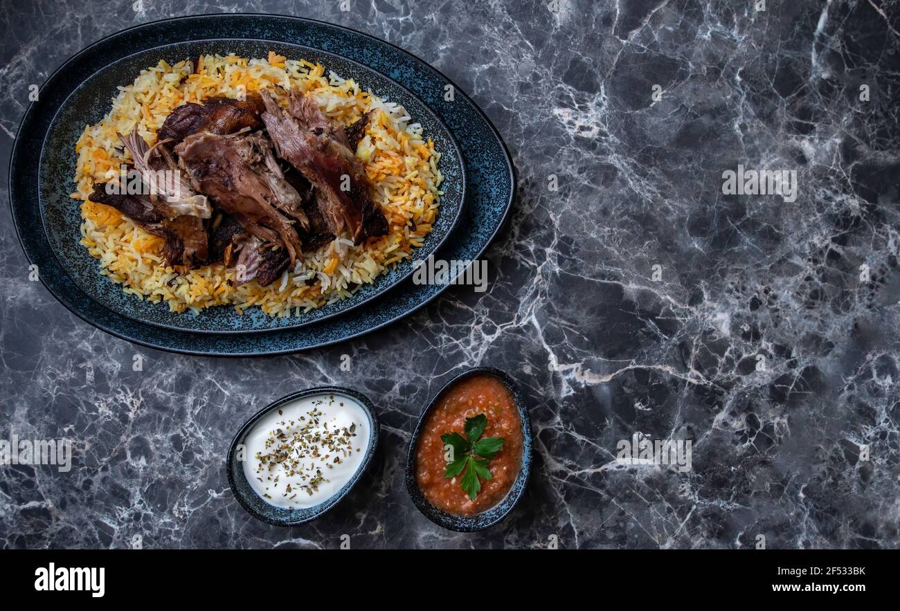 A plate of Kabsa or mandi ,rice and grilled lamb and two small plates of Yogurt and hot sauce. Stock Photo