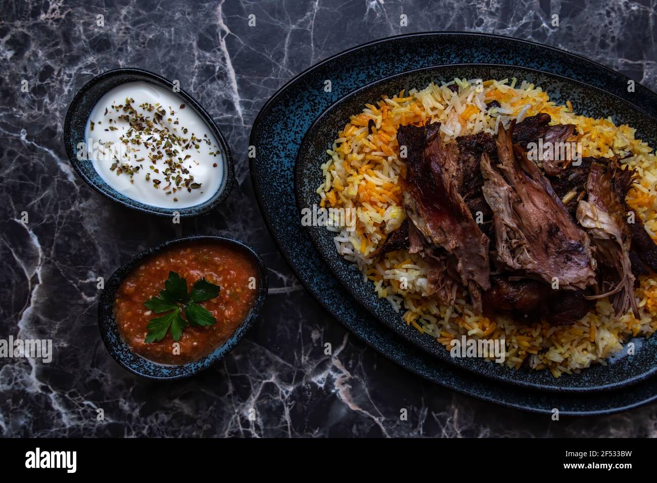 A plate of Kabsa or mandi ,rice and grilled lamb and two small plates of Yogurt and hot sauce. Stock Photo