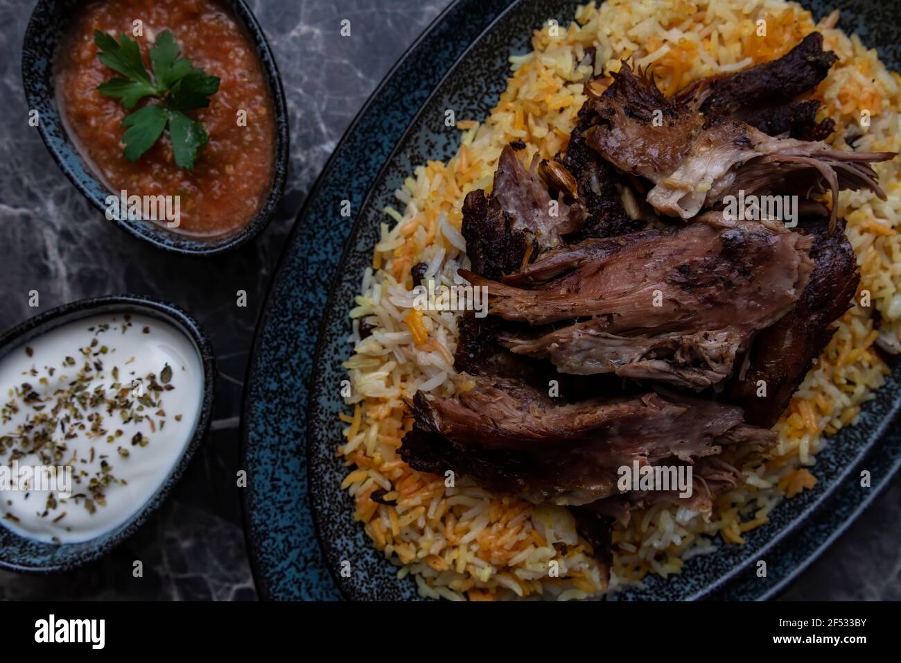 A plate of Kabsa or mandi ,rice and grilled lamb and two small plates of Yogurt and hot sauce. Stock Photo