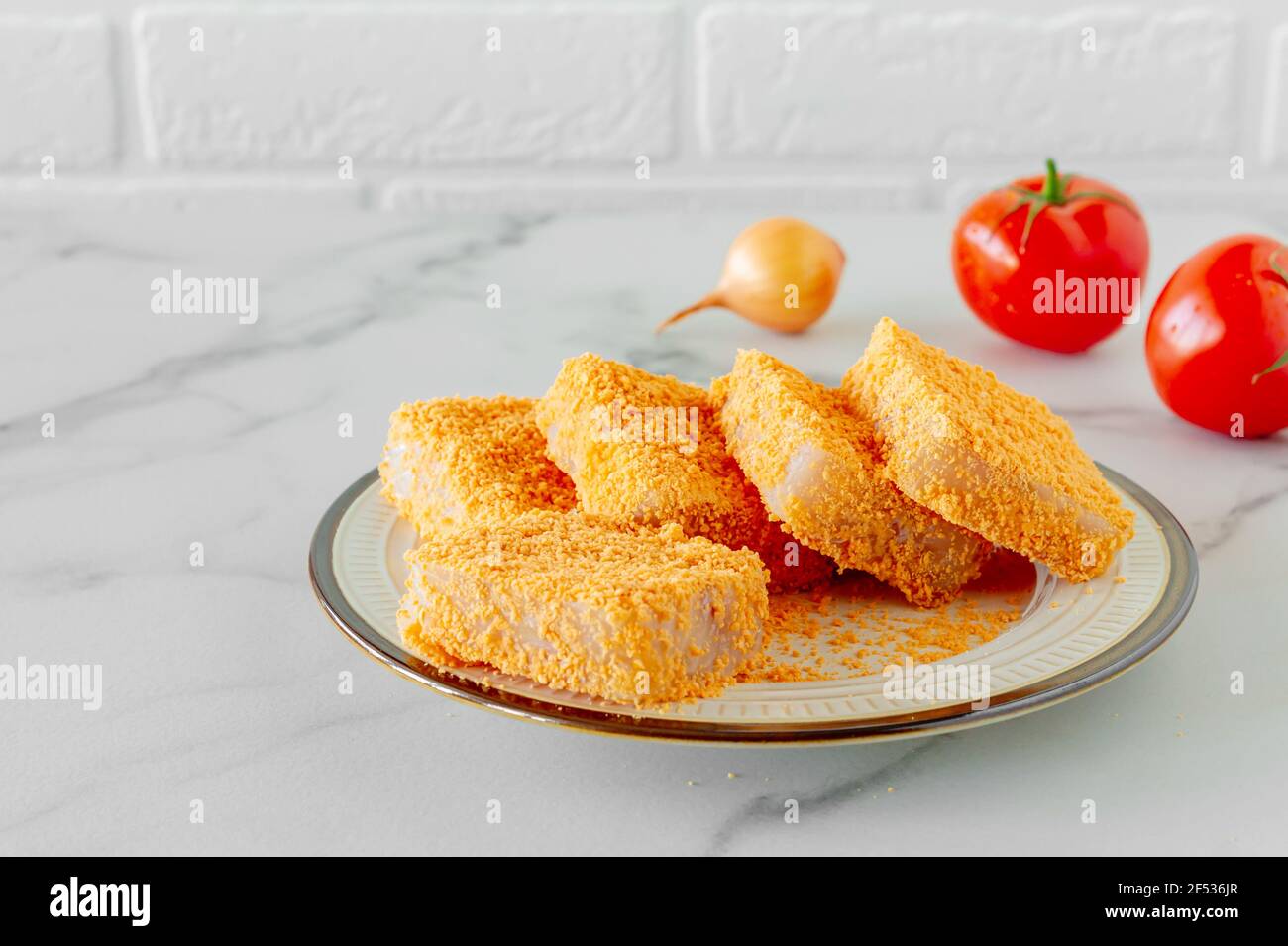 breaded fish patties on a plate prepared to cook. Stock Photo