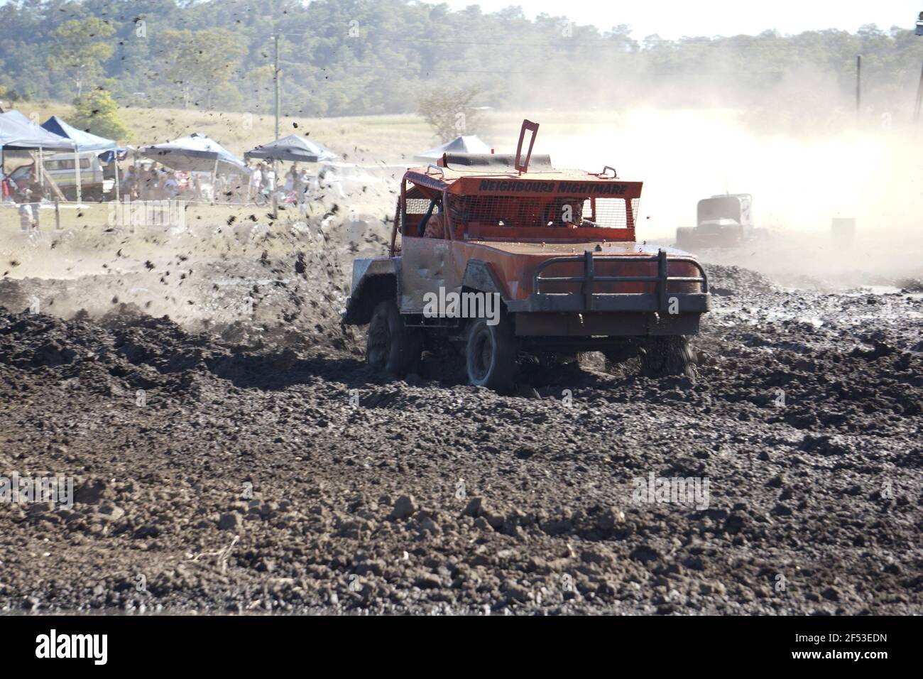 A dented old utility truck taking part in a mud race with everything including the driver covered in dirt and mud. Stock Photo