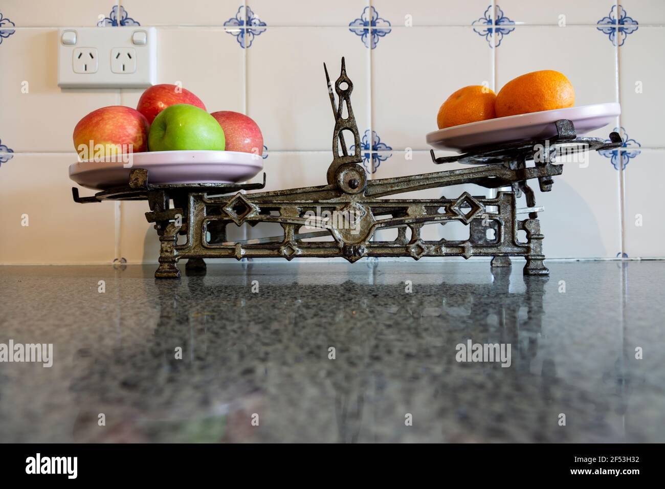 Vintage retro old kitchen iron kitchen scales with red and green apples and oranges on a granite kitchen bench. Stock Photo