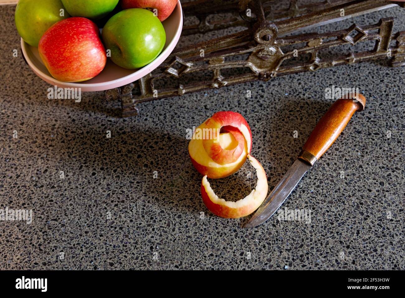 A half peeled apple and a small knife on a kitchen bench with a vintage set of scales and red and green apples. Stock Photo
