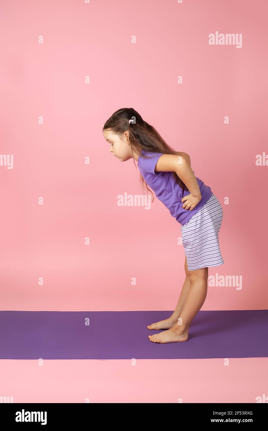 full-length portrait of a girl doing yoga in the Ardha Uttanasana or Standing Half Forward Bend pose, isolated on a pink background Stock Photo