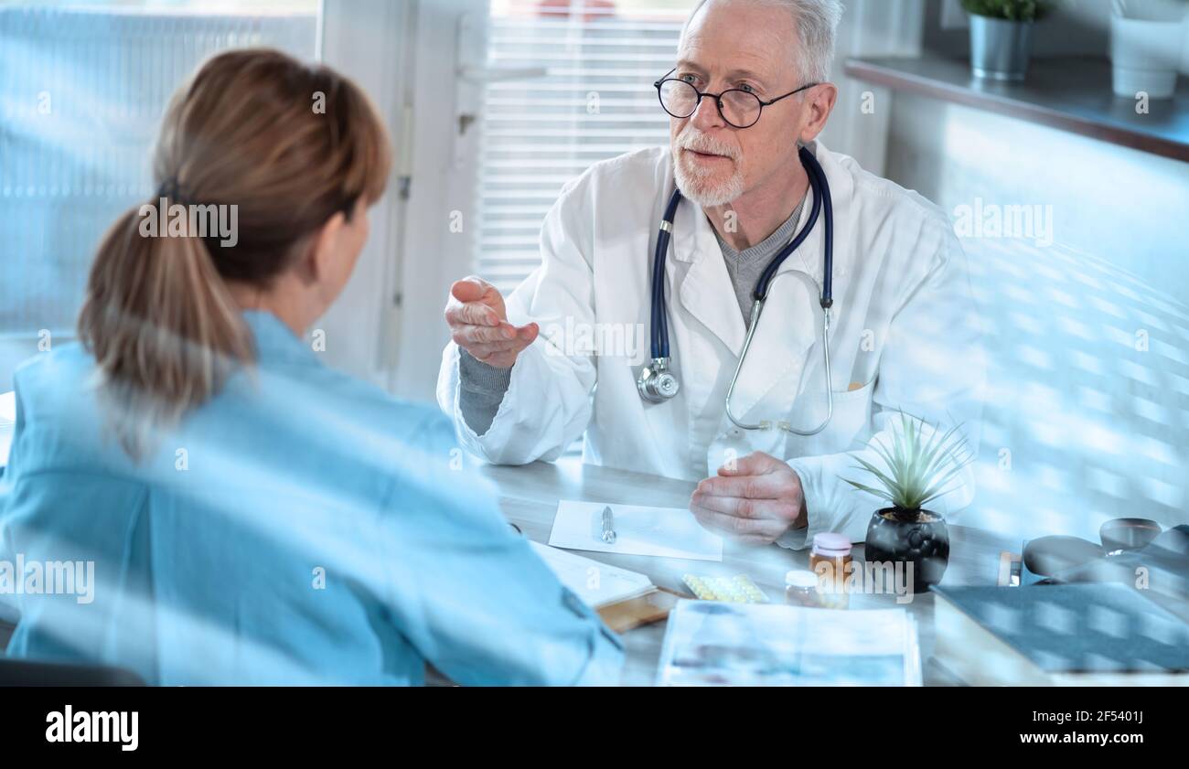 Senior doctor having a discussion with his female patient in medical ...