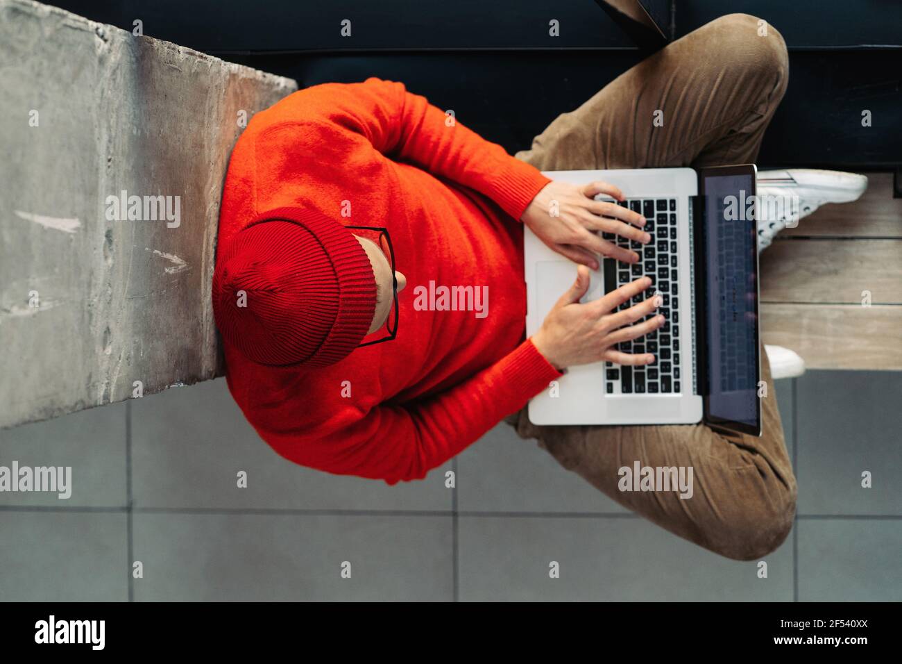 Freelancer man sitting on bench next by window legs crossed, online working on laptop. Distance job Stock Photo