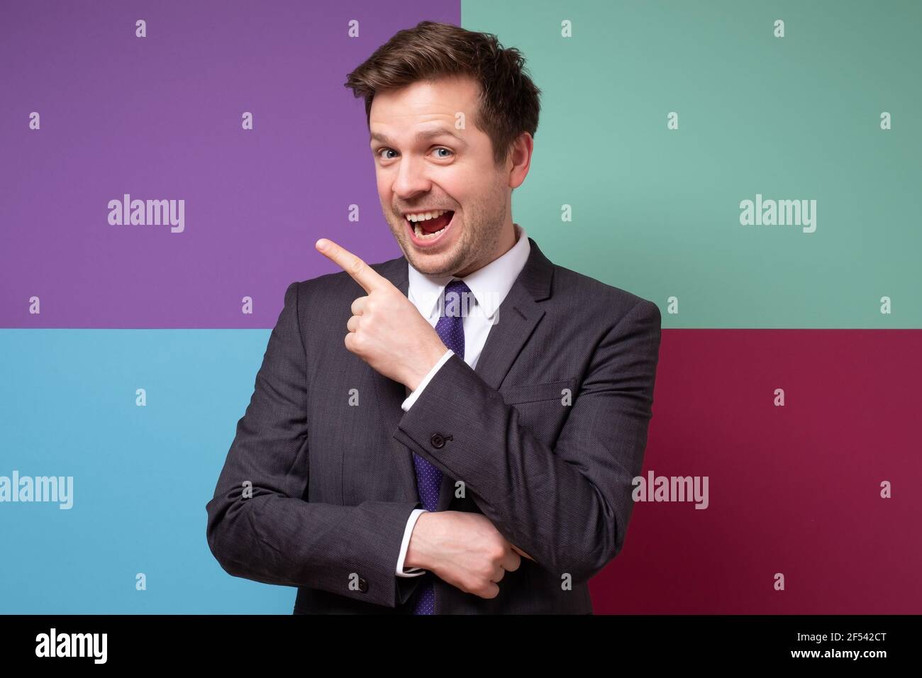 Young excited caucasian businessman with finger point aside. Pay your attention there. Studio shot Stock Photo