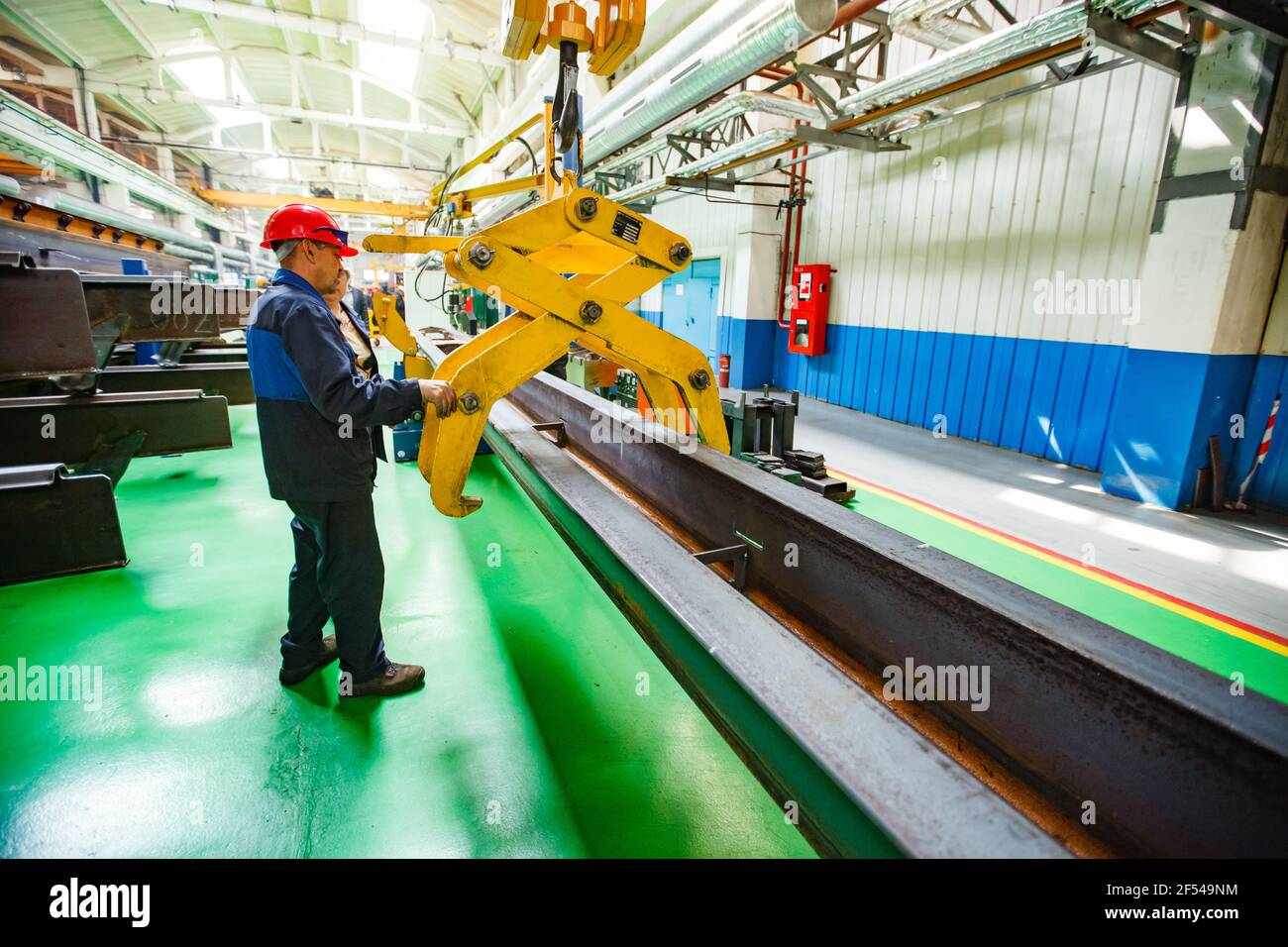 Ekibastuz, Pavlodar region, Kazakhstan - May 28, 2012: Car-building plant. Workers lifting metal rail with overhead crane and mechanical hand. Stock Photo