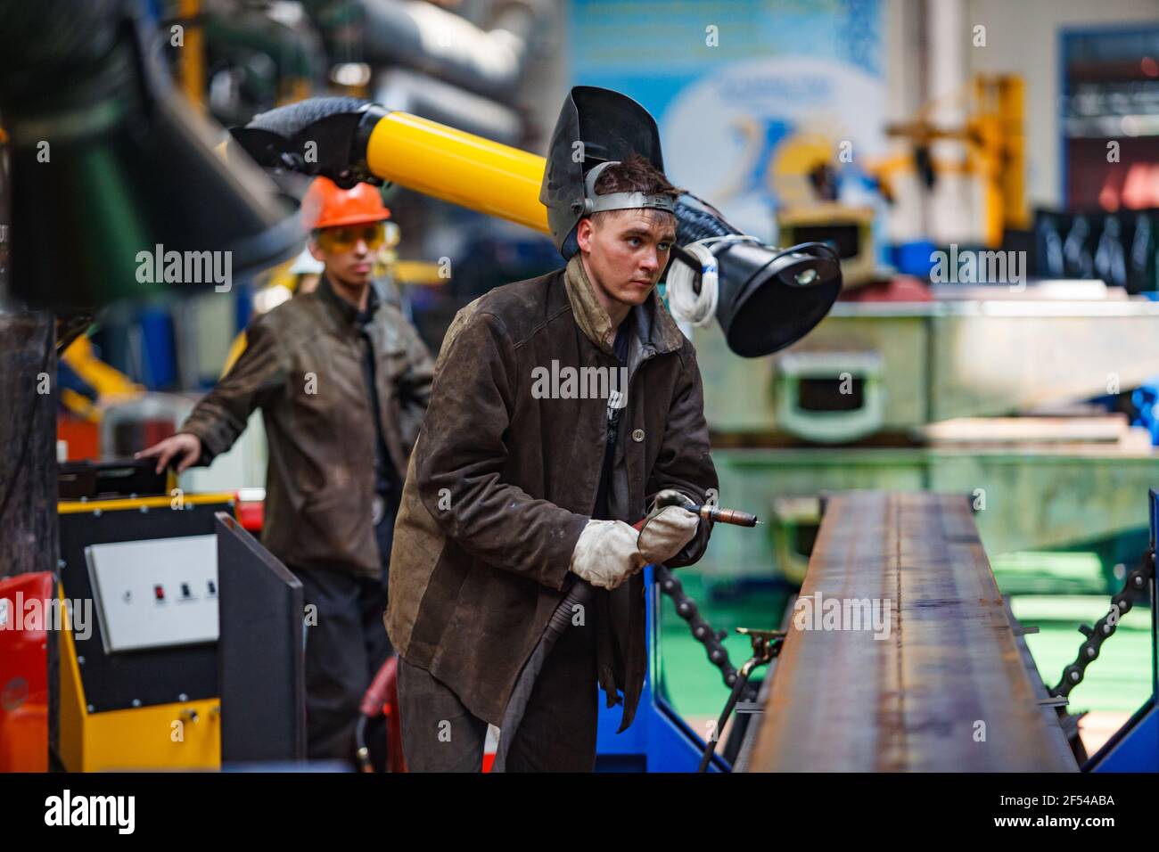 Ekibastuz, Pavlodar region, Kazakhstan - May 28, 2012: Rail car-building plant. Young worker and protective mask. Welding wagon parts with gas-burner. Stock Photo